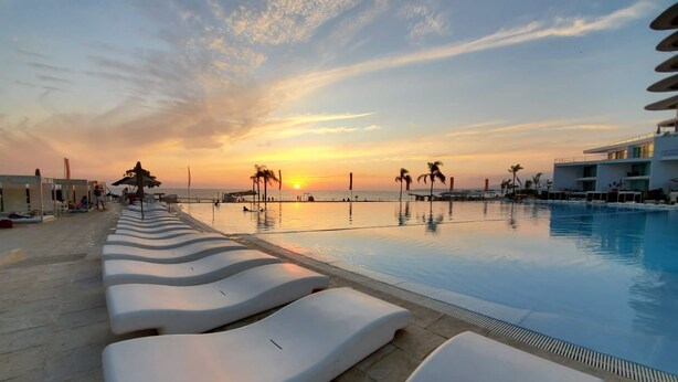 A poolside area with lounge chairs, a sunset view, and a building with balconies.