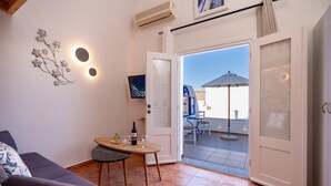 Una sala de estar acogedora con un sofá, una mesita con una botella y vasos, y un balcón con mesa y sillas.