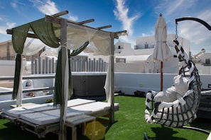 Un salón en la azotea con un toldo, sillones de descanso, una silla colgante y un jacuzzi.