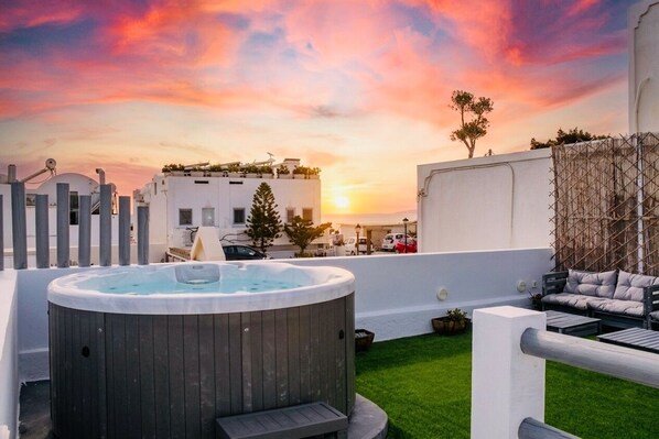 Una terraza en la azotea con jacuzzi, mobiliario exterior y vistas al atardecer.