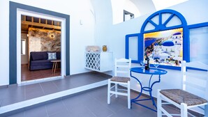 Un interior moderno con una zona de estar que incluye sillas blancas y una mesa azul, una pared decorada con un cuadro, y una puerta que conduce a otra habitación.