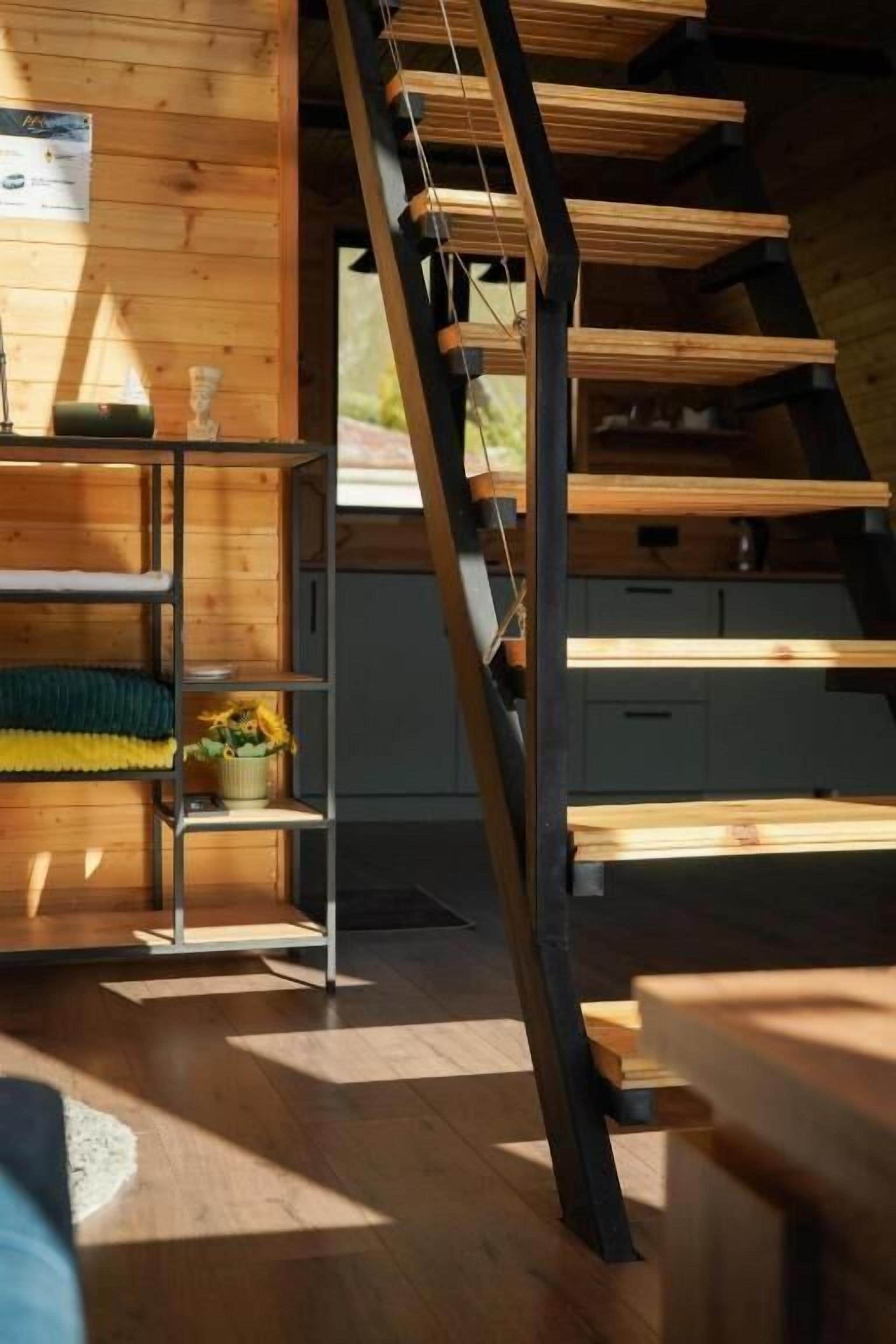 Un interior de madera con una escalera, una estantería con plantas y vistas al exterior.