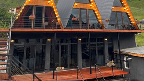 A modern building with a triangular roof design, large windows, and a wooden deck. - PYRAMID KAZBEGI (Kazbegi)