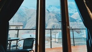 A room with a sloped wooden ceiling and large windows offering a view of snow-capped mountains. - PYRAMID KAZBEGI (Kazbegi)