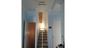 Een trap die leidt naar een deur met daarop 'Entrée', met een lamp erboven.