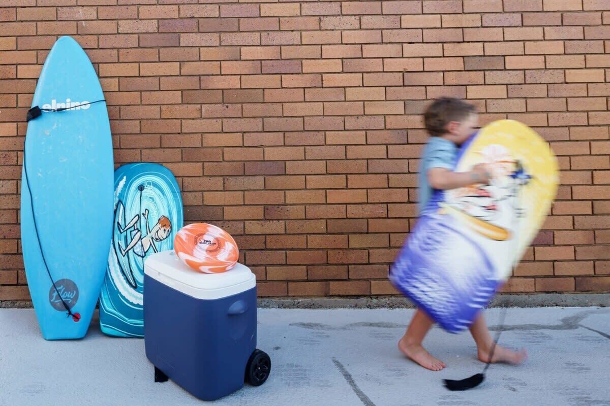 A child walking past surfboards and a cooler.