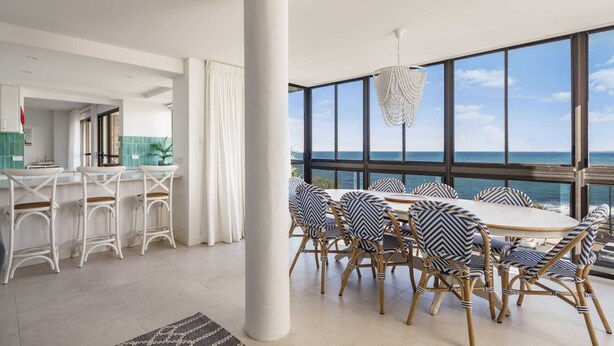 A modern dining area with a large table and chairs, a white pillar, and a view of the ocean. - Absolute Beachfront Bliss on Kings Beach (Kings Beach)