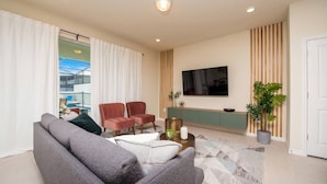 A modern living room with a sofa, chairs, a TV, and a potted plant.