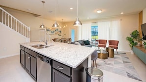 A kitchen with a granite countertop, stainless steel appliances, pendant lighting, and a dining area with a table and chairs.