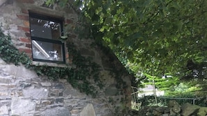 Un bâtiment rustique en pierre, doté d’une petite fenêtre, d’une table en métal vert et de deux chaises en bois.