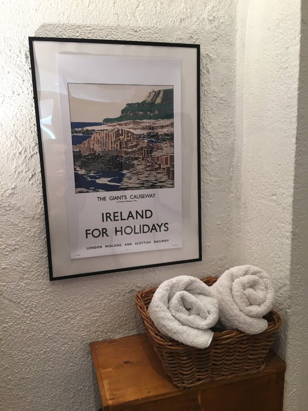 A framed print of 'The Giant's Causeway' with a basket of white towels below.