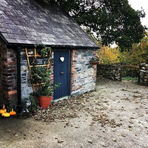 A rustic cottage with a blue door, a wooden ladder, and a heart-shaped decoration. - The Gardener's Cottage (Ballynahinch)