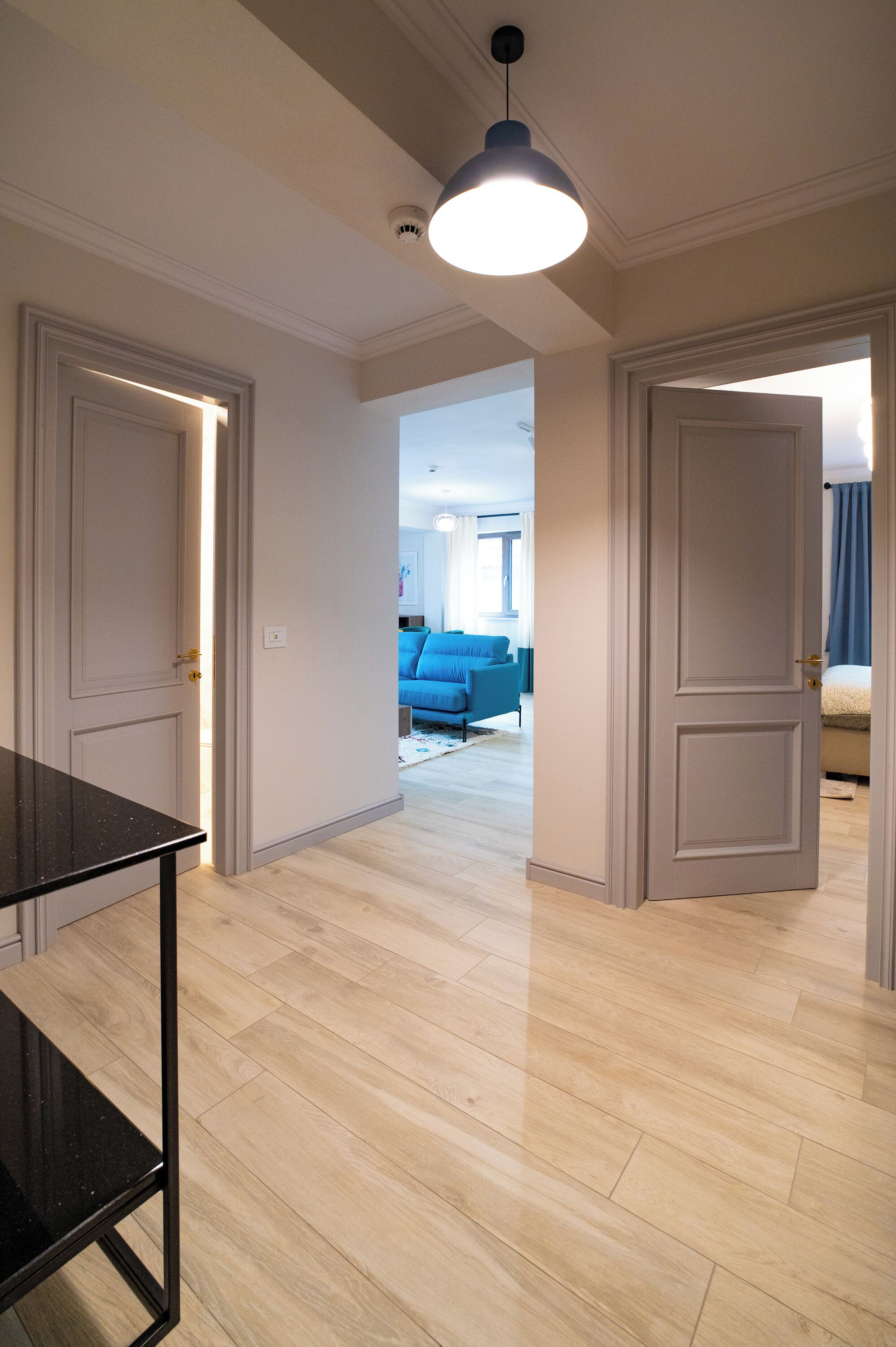 Un couloir doté d’un plancher en bois, de deux portes fermées et d’une table dont le plateau est noir.