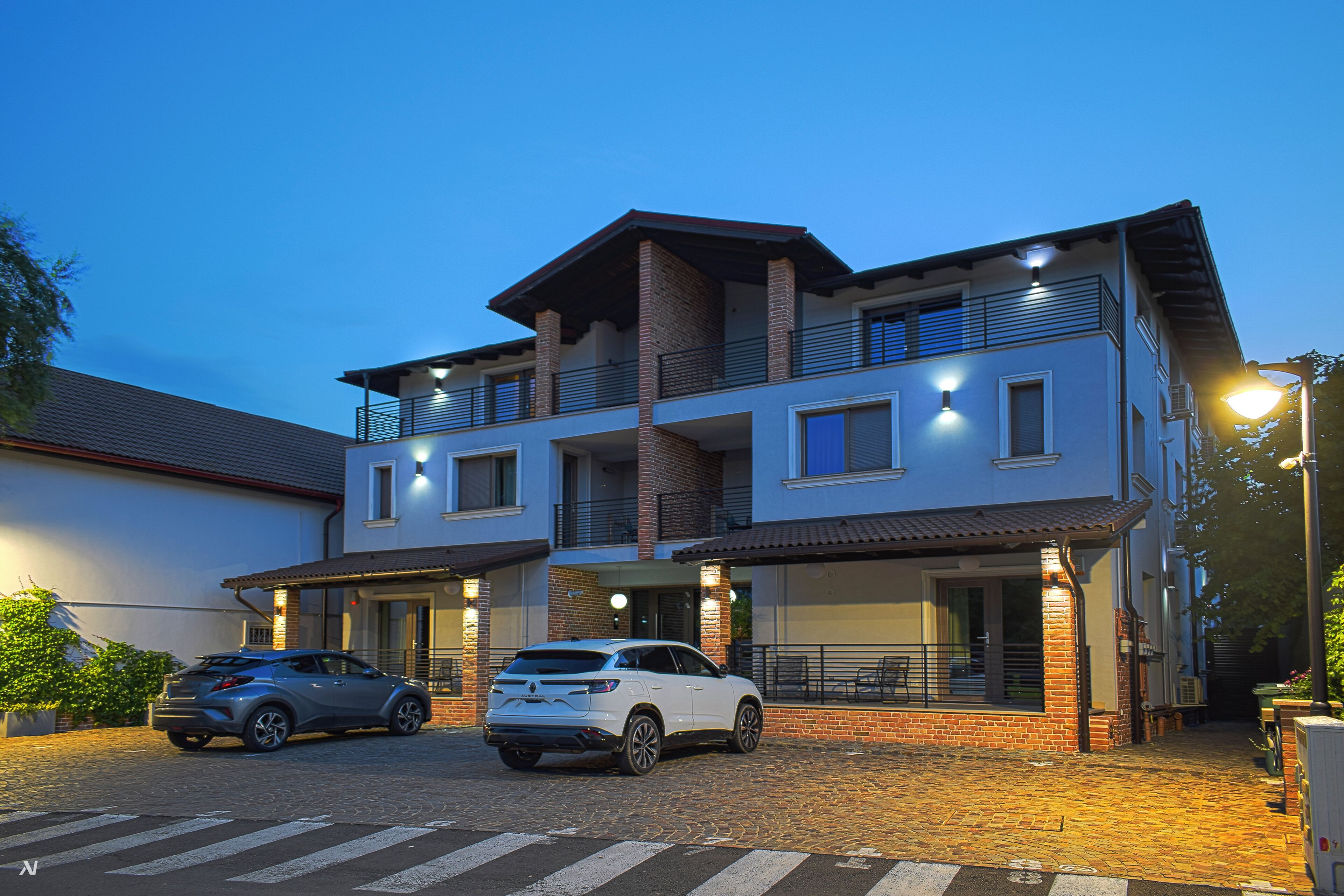 A modern two-story building with a carport, featuring a brick facade, multiple balconies, and a flat roof.