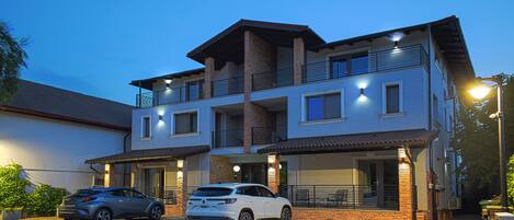 A modern two-story building with a carport, featuring a brick facade, multiple balconies, and a flat roof.