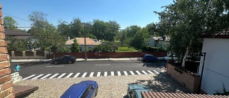A residential street with two parked cars, a pedestrian crossing, and houses with brick walls and tiled roofs.