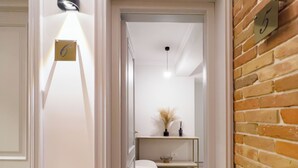A hallway with a white door, a number 6 sign, a small table with a vase, and a brick wall.
