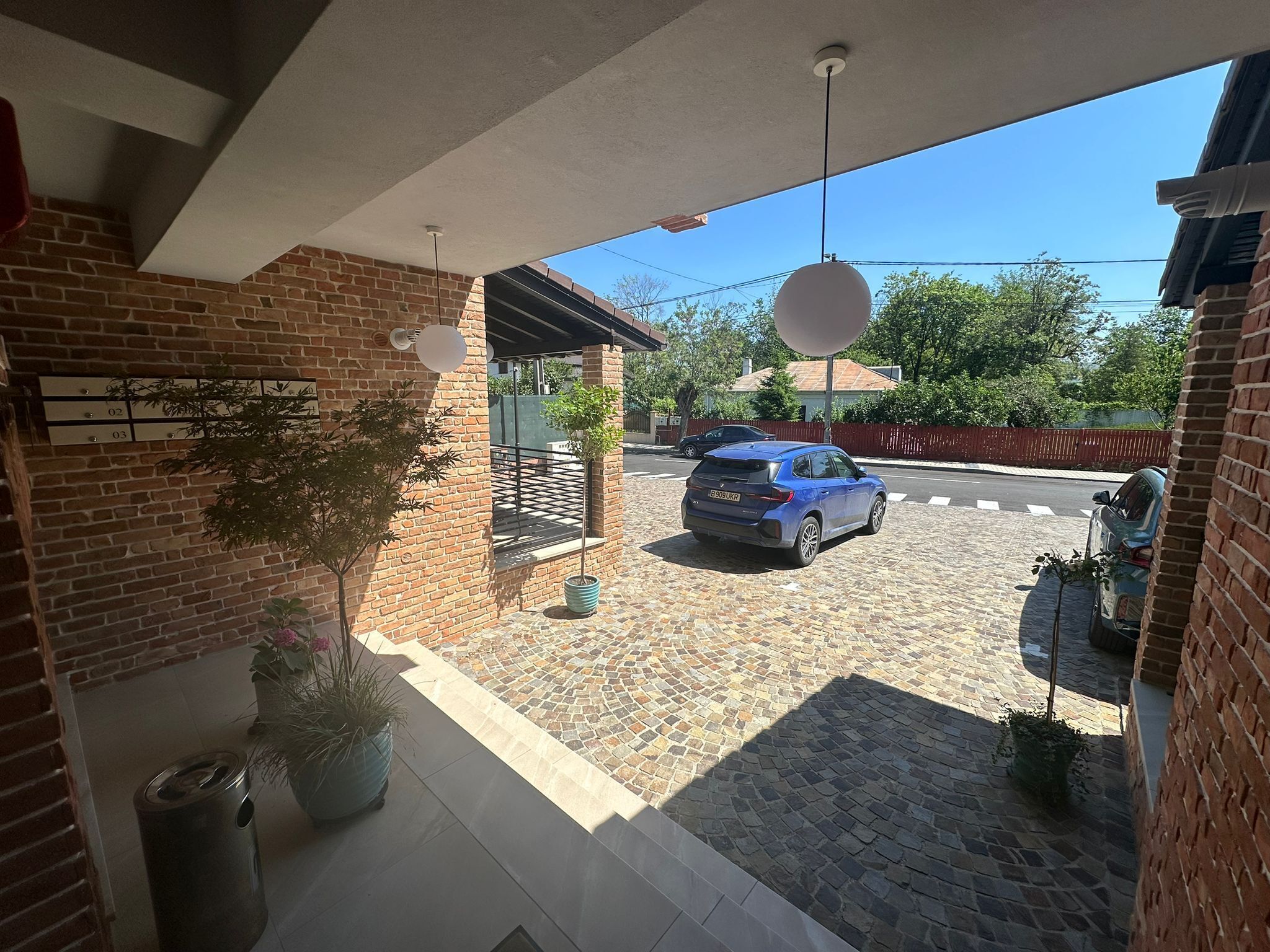 Una casa de ladrillo con un patio empedrado, un coche aparcado y un árbol pequeño.