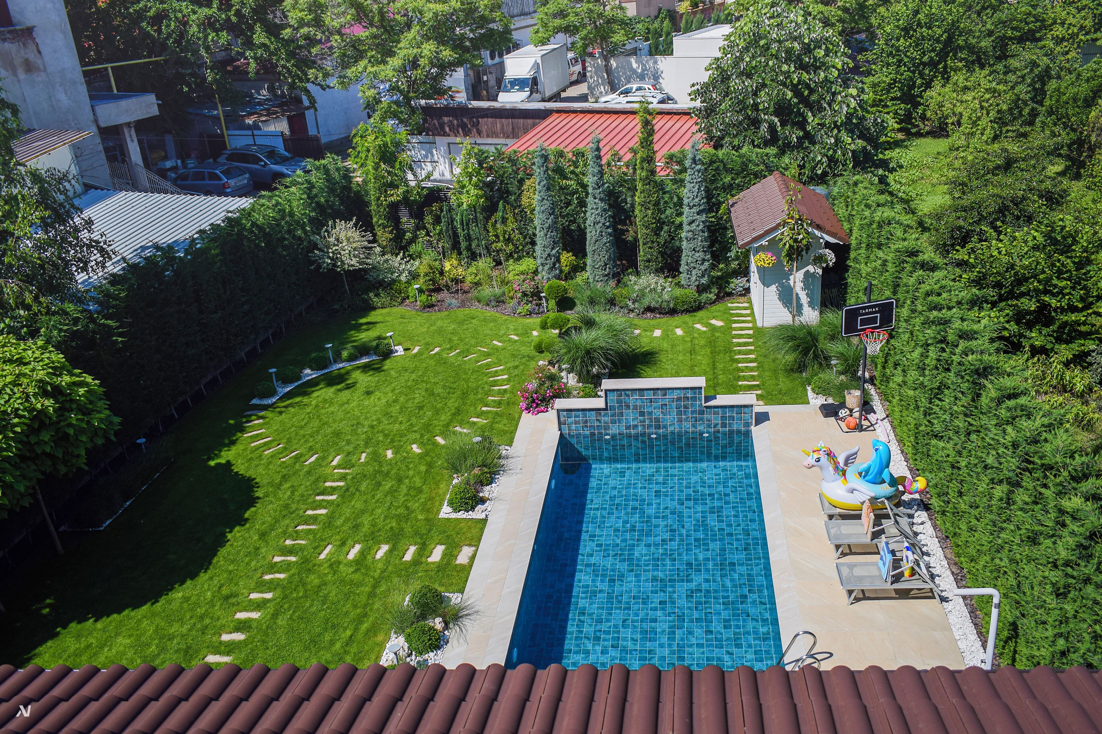 Une piscine dotée d’une terrasse carrelée, entourée d’une pelouse bien entretenue et d’un petit jardin agrémenté d’un abri de jardin.
