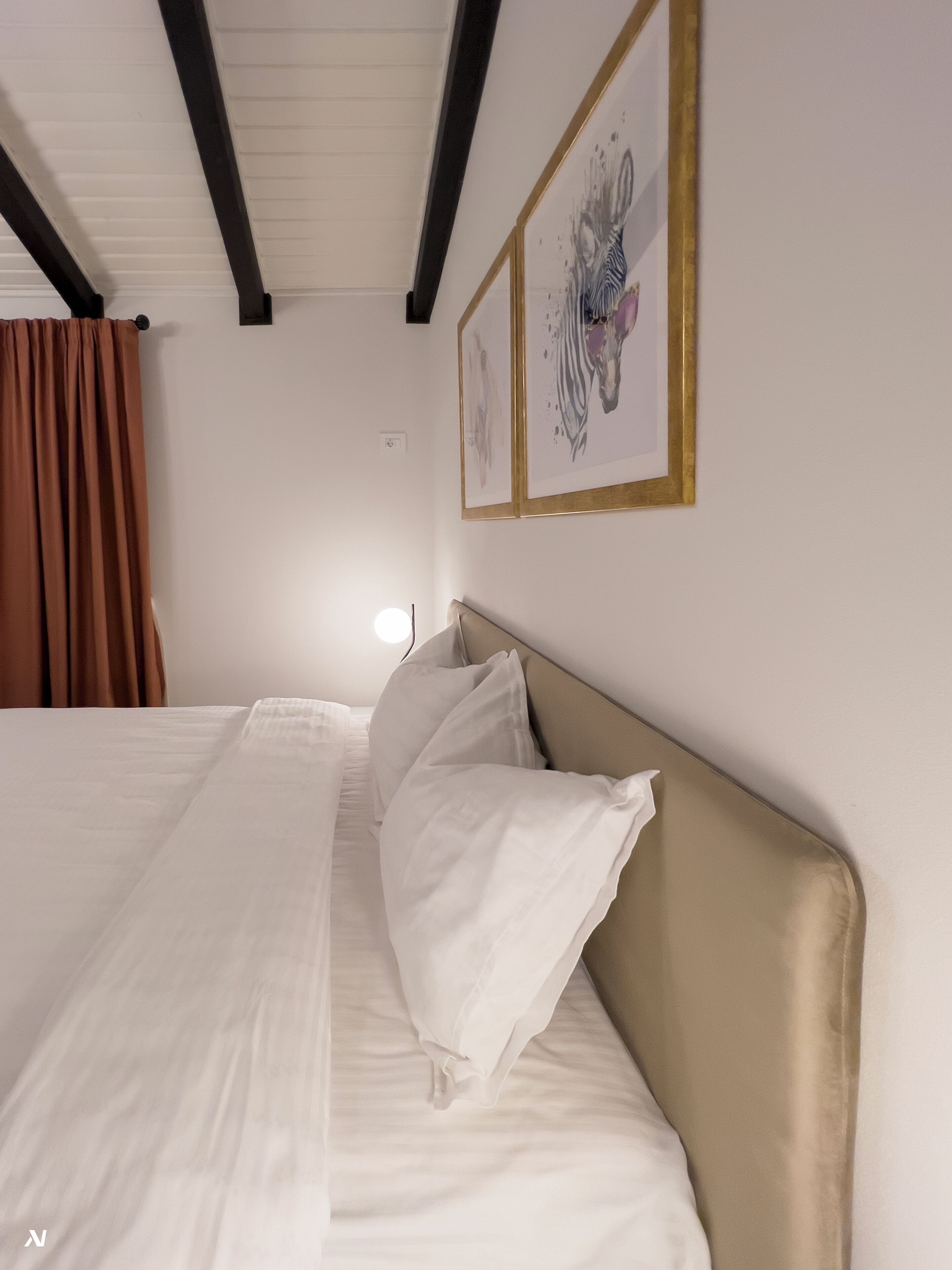 Una cama bien tendida con sábanas blancas y un cabecero color beige en una habitación con paredes blancas y techo inclinado.
