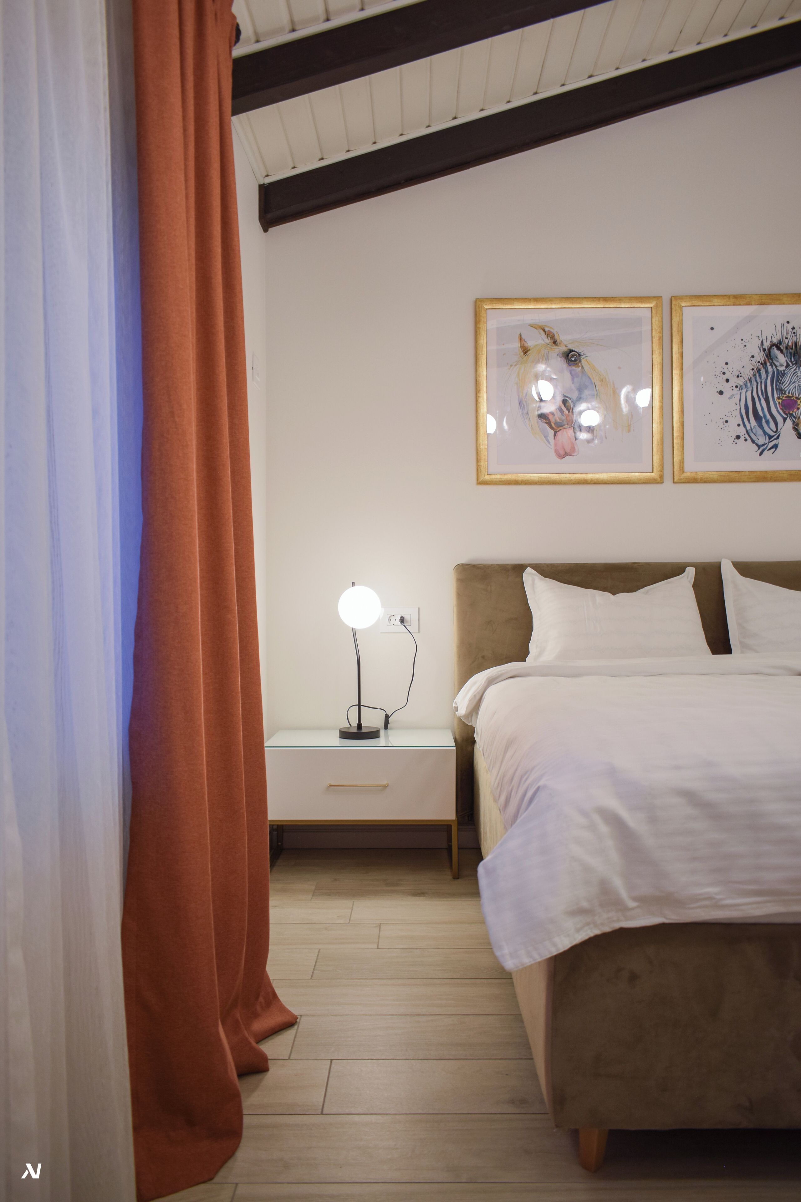 Ein Schlafzimmer mit einem Bett, einem Nachttisch mit Lampe und zwei gerahmten Kunstwerken an der Wand.