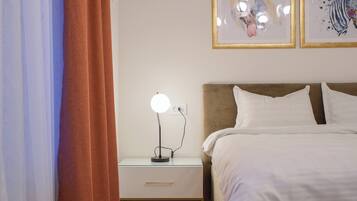 A bedroom with a bed, a nightstand with a lamp, and two framed artworks on the wall.