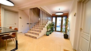 A staircase with patterned steps leading to a landing, a dining area with a table and chairs, and potted plants along the hallway.