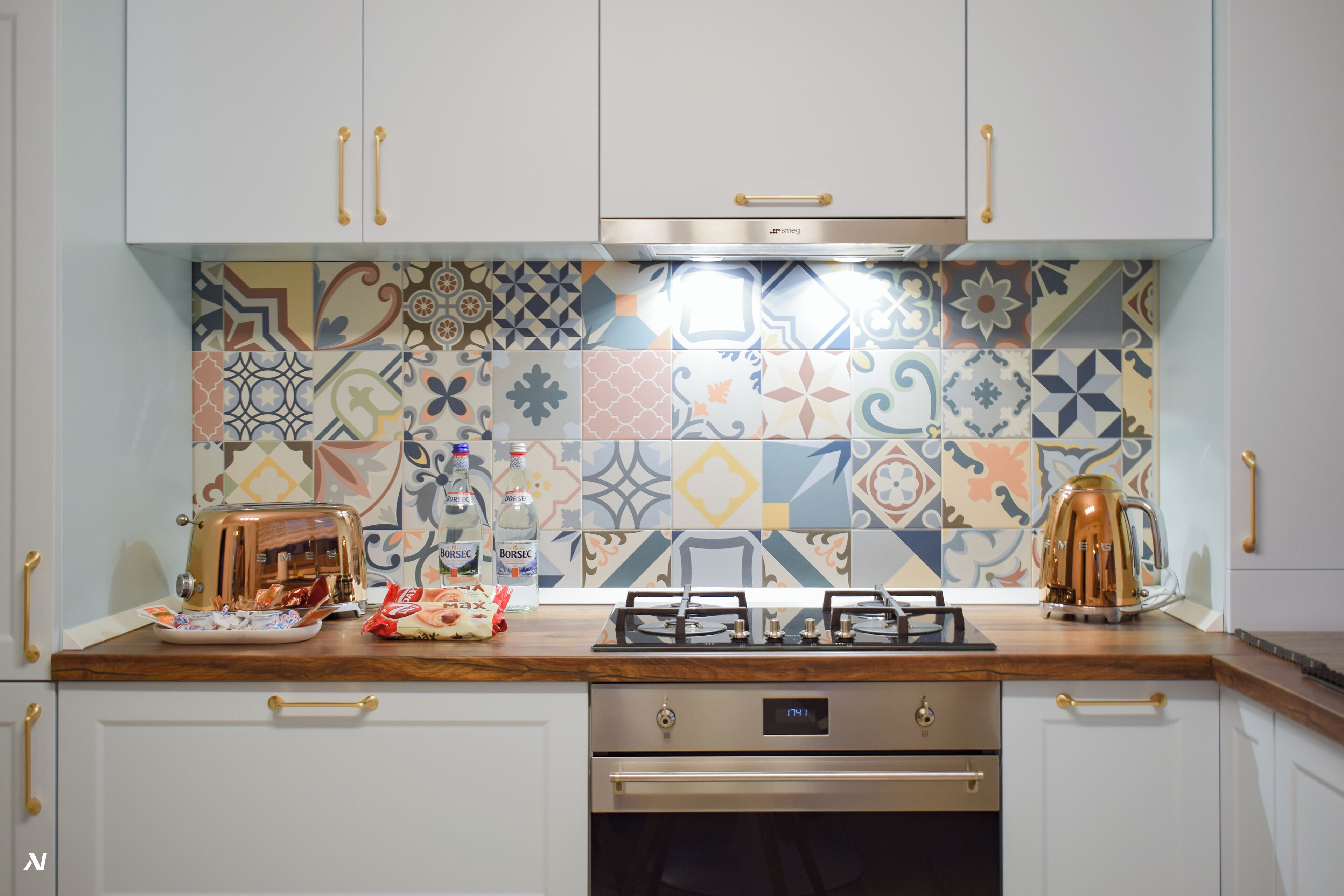 A kitchen with white cabinets, a stainless steel range hood, and a colorful tile backsplash.