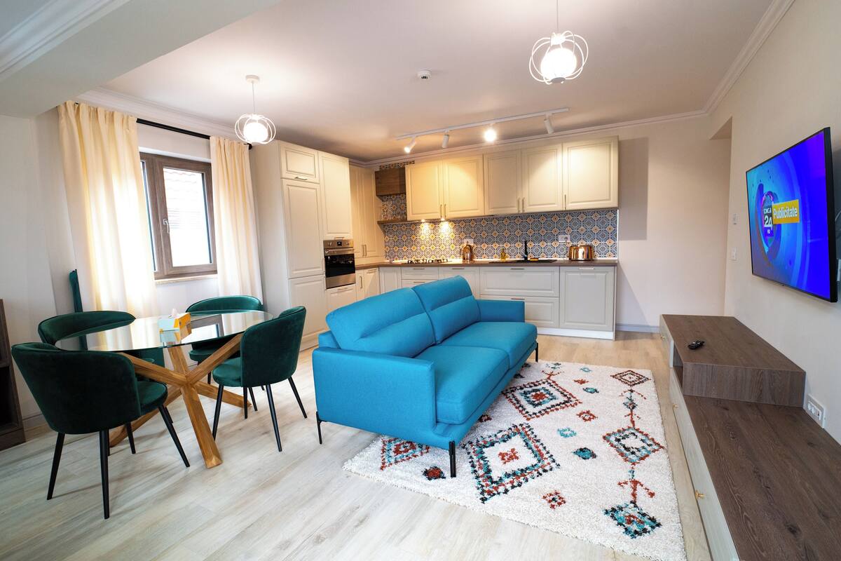 A modern living room with a blue sofa, green chairs, a glass coffee table, and a patterned rug.