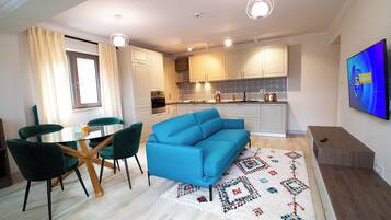 A modern living room with a blue sofa, green chairs, a glass coffee table, and a patterned rug.