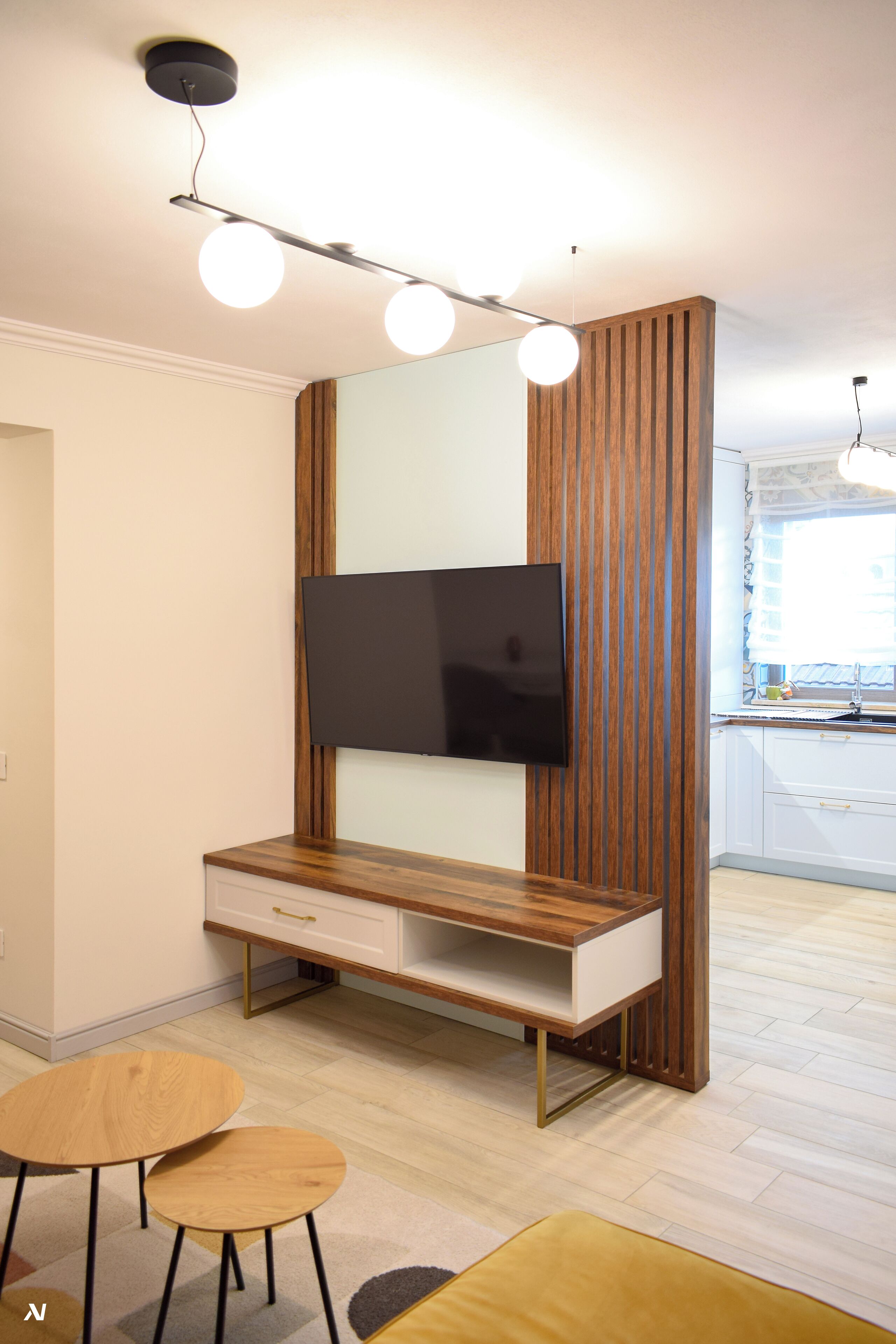 A modern living room with a flat-screen TV mounted on a wooden panel wall, a wooden coffee table, and a small dining table.