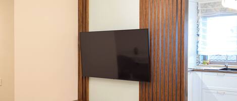 A modern living room with a flat-screen TV mounted on a wooden panel wall, a wooden coffee table, and a small dining table.