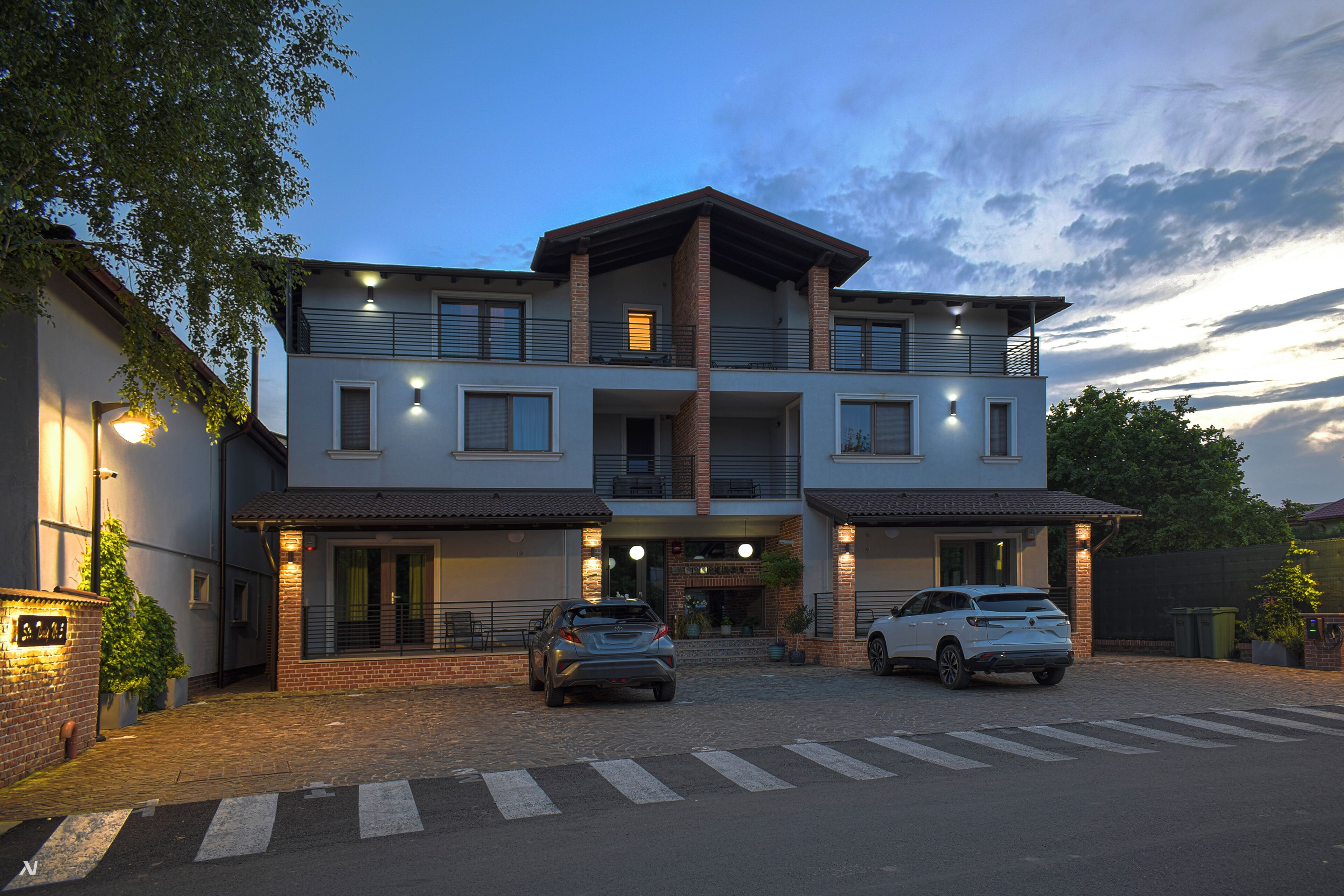 Ein modernes, zweistöckiges Gebäude mit Ziegelaußenwand, zwei Autos vor der Fassade und einem Fußgängerüberweg zum Eingang.