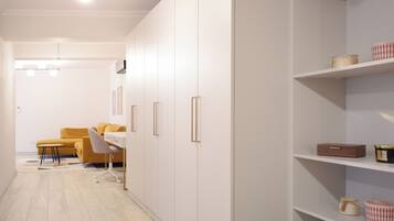 A modern, minimalist room with white walls, a wooden floor, a yellow sofa, a desk, and a shelving unit with decorative items.