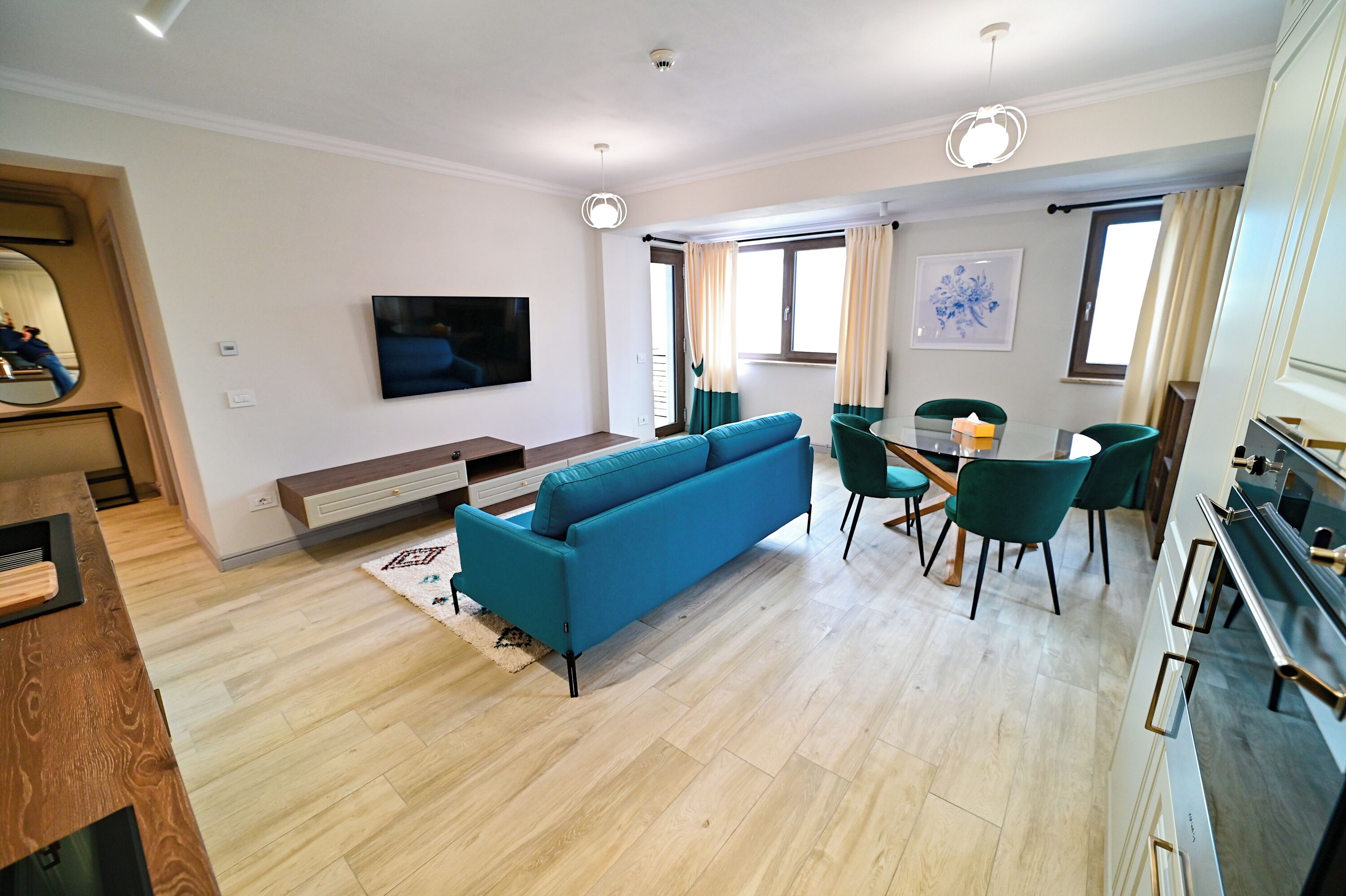 Een moderne woonkamer met een blauwe bank, een eethoek met groene stoelen, en een keuken met een zwarte kookplaat.