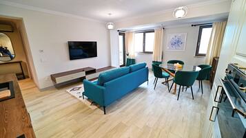 Een moderne woonkamer met een blauwe bank, een eethoek met groene stoelen, en een keuken met een zwarte kookplaat.
