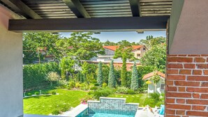 A patio with a round table and two chairs, overlooking a swimming pool and a garden.