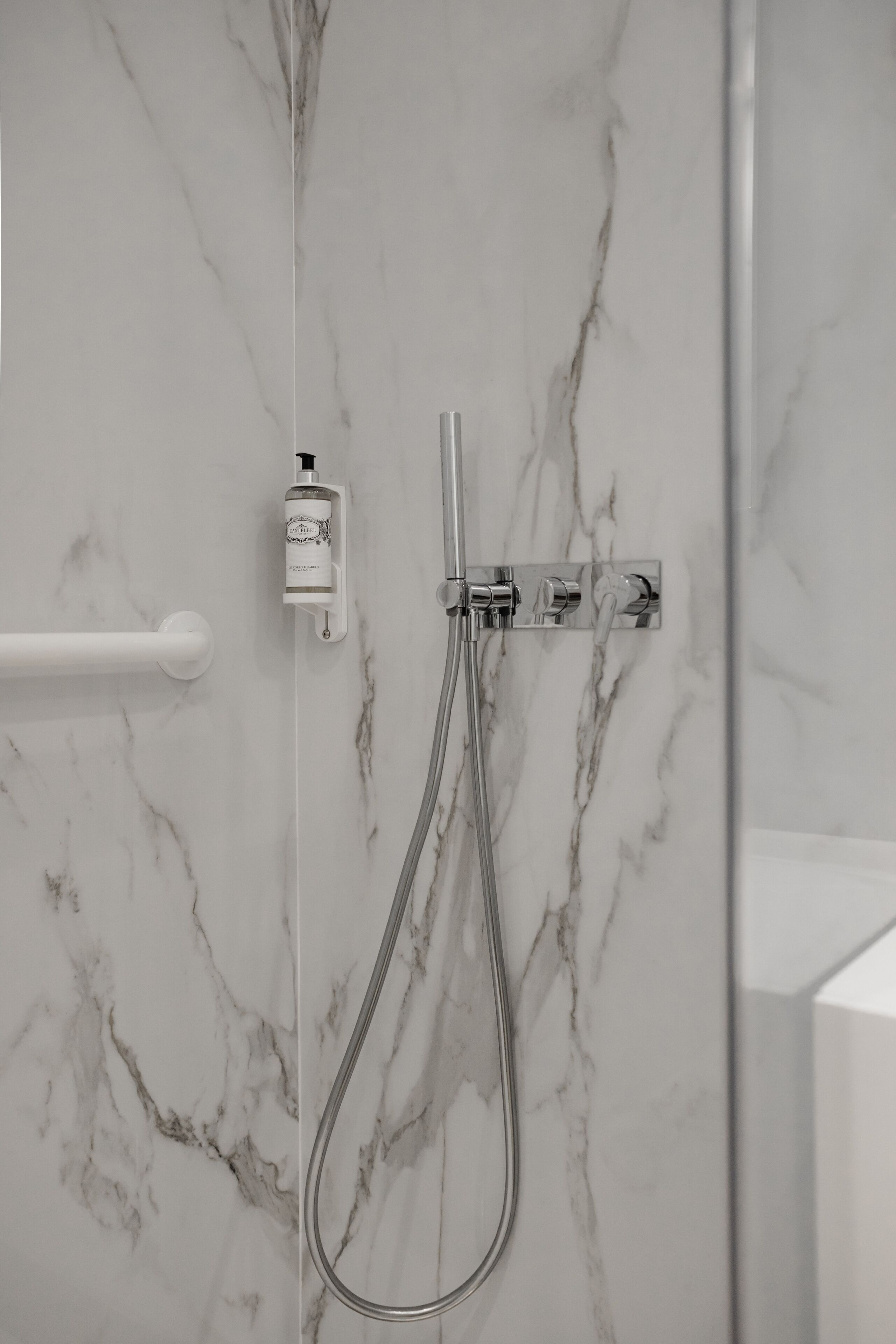 Une salle de bain avec un mur en marbre, une douche équipée d’un pommeau de douche amovible et un flacon de gel douche Castelfelso.