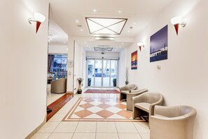 A hotel lobby with a check-in desk, seating area, and a view of the street through the glass doors. - Villa Maria (Cesenatico)