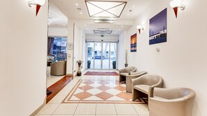 A hotel lobby with a check-in desk, seating area, and a geometric ceiling design. - Villa Maria (Cesenatico)