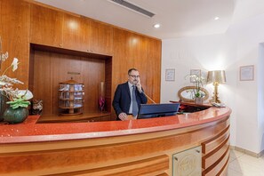Un comptoir d’accueil avec un revêtement en bois, un téléphone et un ordinateur. On y trouve également des vases décoratifs et un miroir accroché au mur.