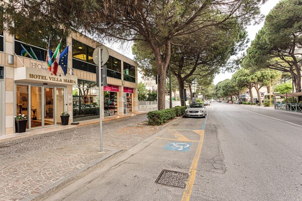 A hotel with a storefront, outdoor seating, and a parking area with a handicapped parking space. - Villa Maria (Cesenatico)