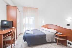 A hotel room with a bed, a desk with a television, a chair, a bedside table with a phone, and a window with curtains. - Villa Maria (Cesenatico)