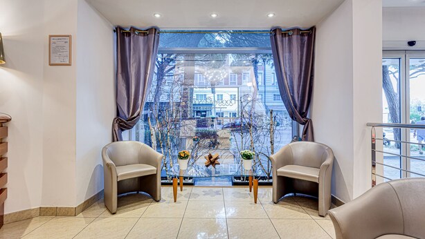 A hotel lobby with two leather chairs, a glass partition, and a view of the cityscape through large windows. - Villa Maria (Cesenatico)