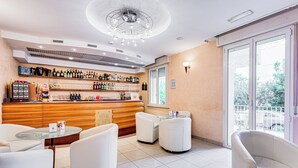 A modern bar area with a wooden counter, various bottles, and a seating area with white chairs and a glass table. - Villa Maria (Cesenatico)
