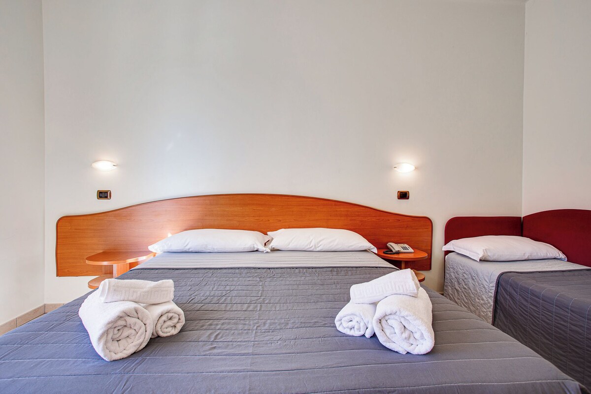 Une chambre d’hôtel avec un grand lit, deux tables de chevet et un fauteuil rouge recouvert de tissu.