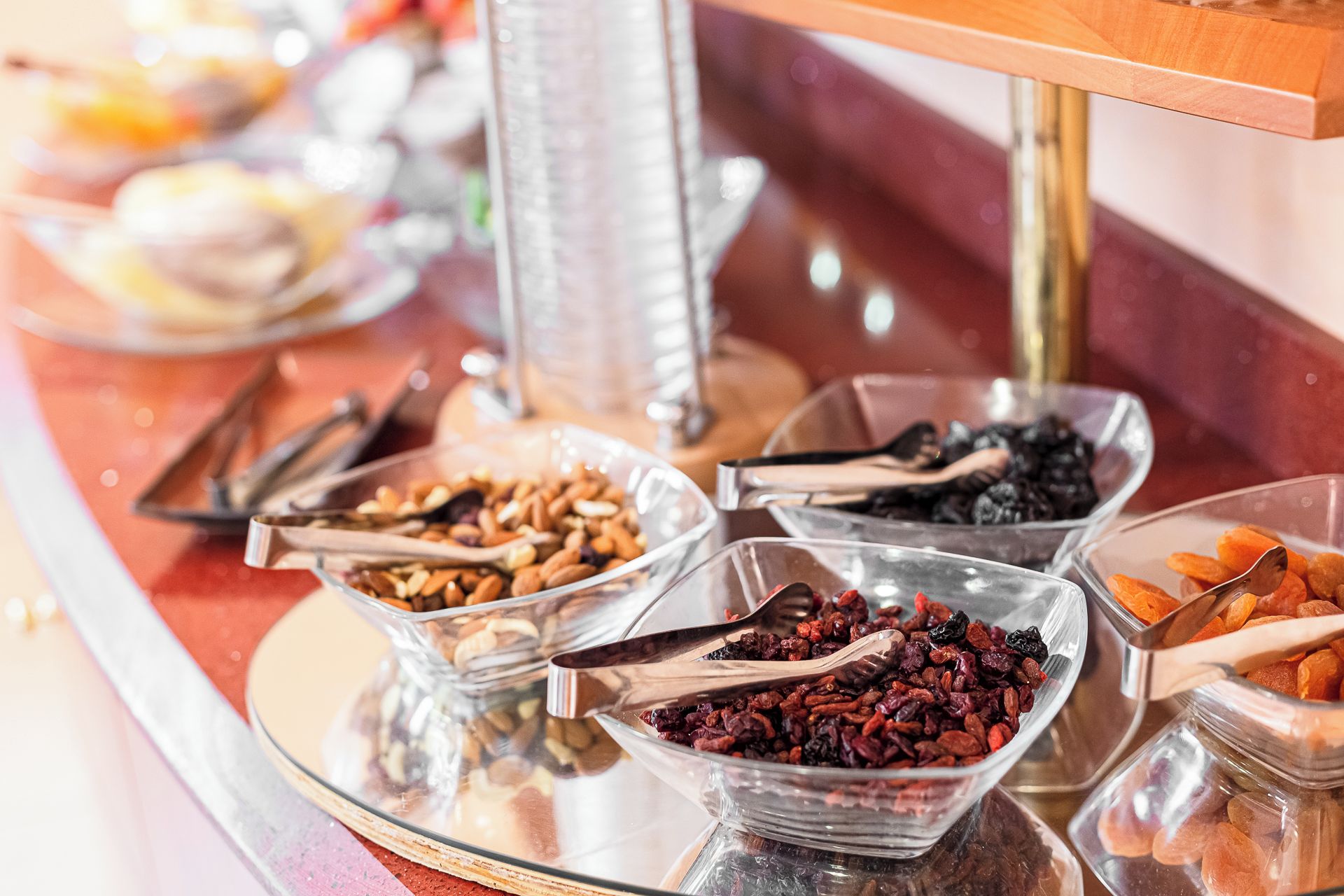Un buffet con diversi cibi esposti in ciotole di vetro, tra cui frutta secca, noci e altri snack.