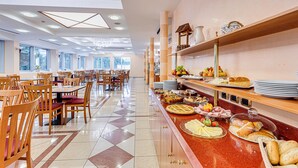 A spacious dining area with multiple tables and chairs, a buffet counter with various food items, and large windows allowing natural light. - Villa Maria (Cesenatico)