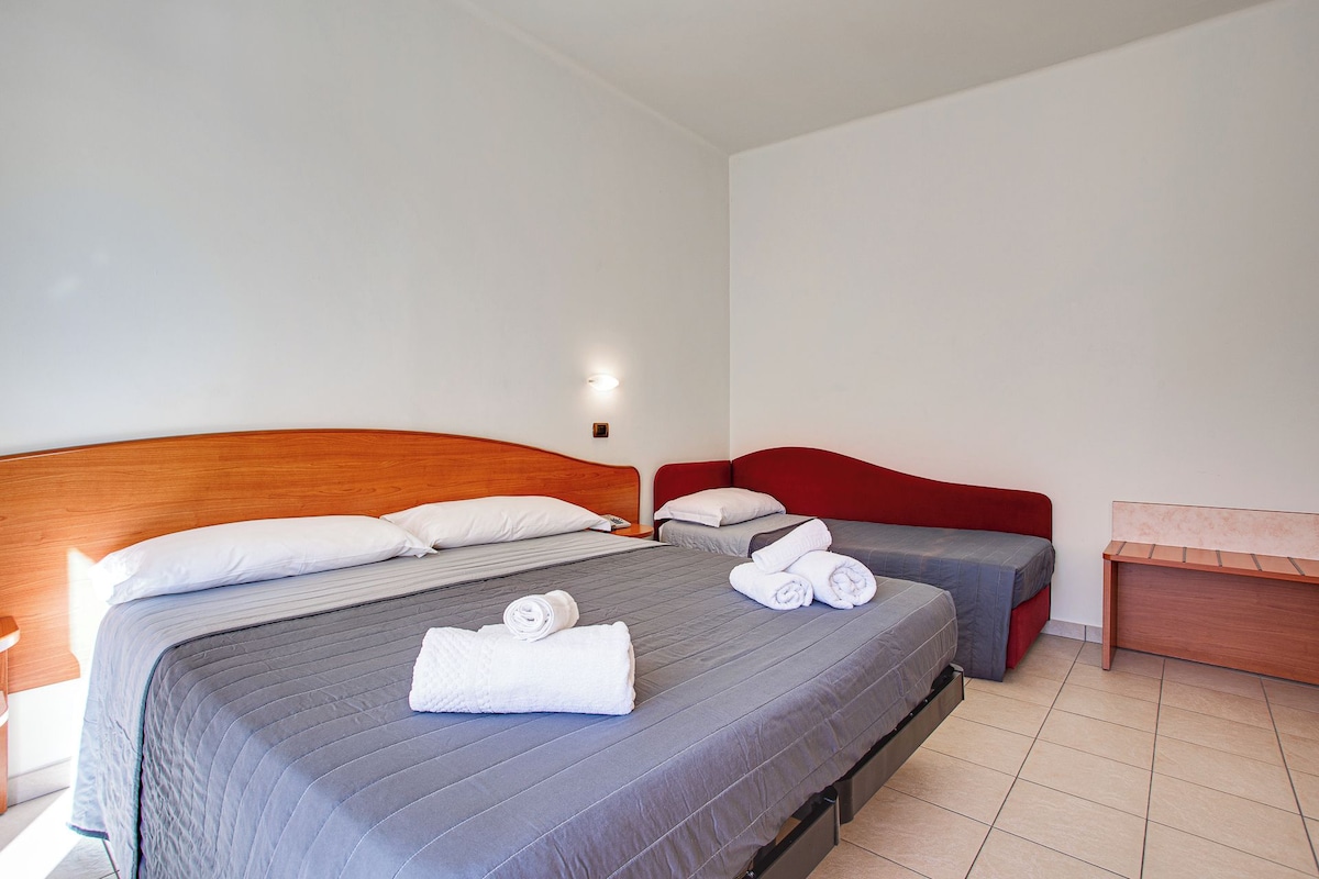 Una habitación de hotel con dos camas, cabecero de madera, cabecero tapizado rojo y un pequeño escritorio de madera.