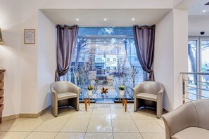 A hotel lobby with two leather chairs, a glass partition, and a view of the cityscape through large windows. - Villa Maria (Cesenatico)